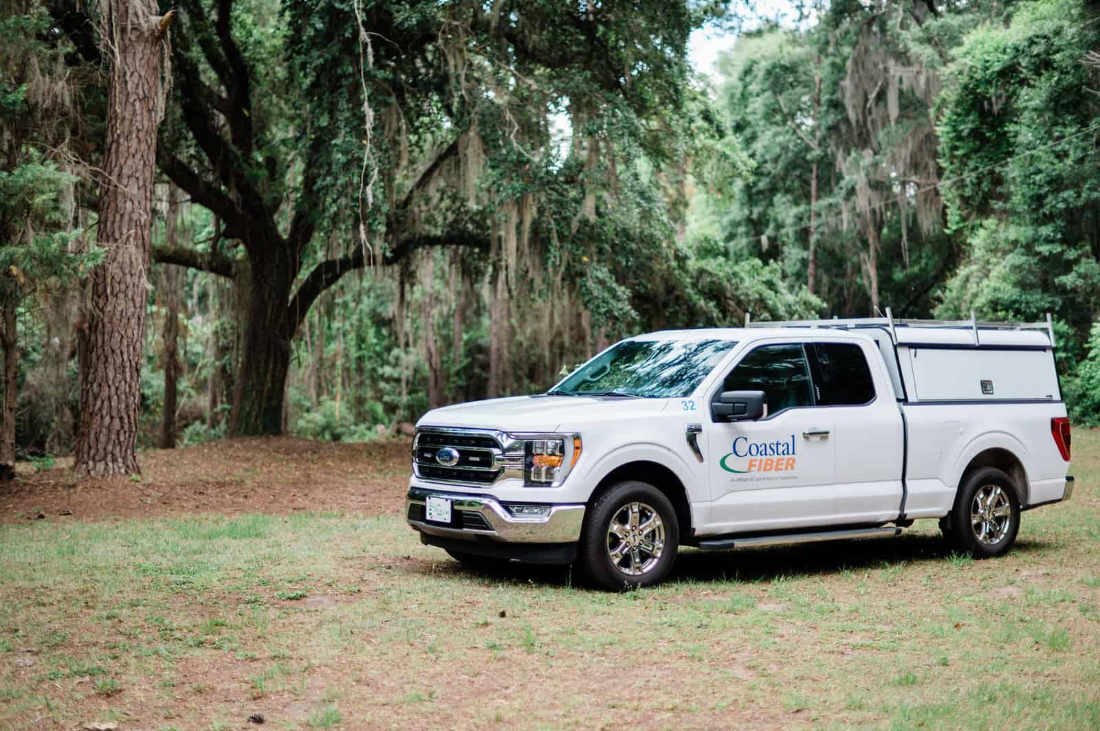 White Coastal Fiber service truck with local marsh and pier in the background.