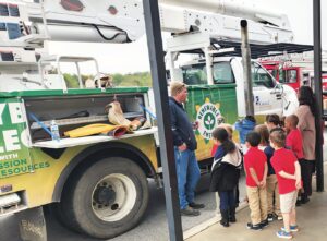 Mr. Duke in front of a Coastal Electric Cooperative utility truck with children and teacher looking on