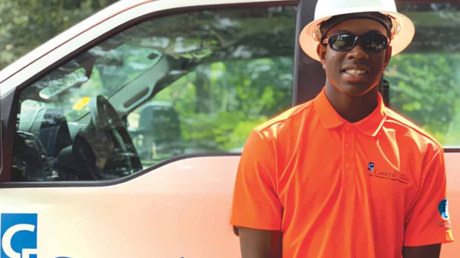 Smiling young man wearing hardhat and orange Coastal Electric Cooperative polo shirt