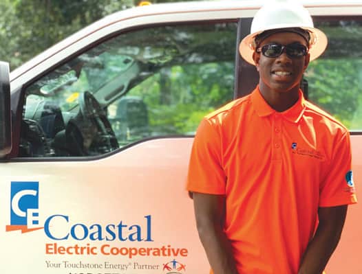 Smiling young man wearing a hardhat and orange Coastal Electric Cooperative polo shirt