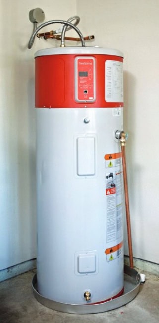 A tall, cylindrical water heater with a red and gray body stands in a corner, featuring various controls and copper piping attached.