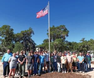 Coastal Electric staff and student volunteers stand proudly near the flagpole raised on historic Oglethorpe Square.